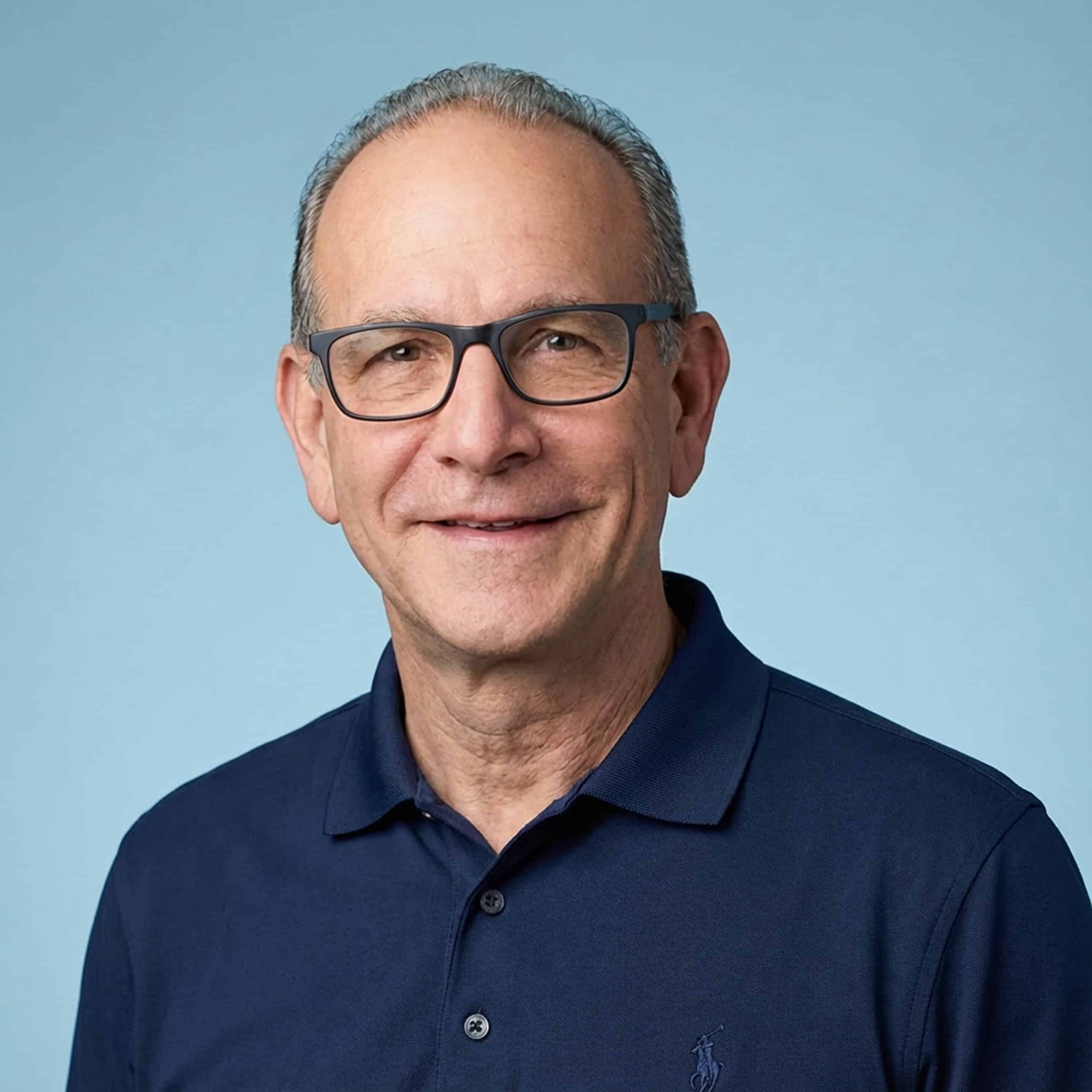 Smiling man wearing glasses and a navy polo shirt against a light blue background.